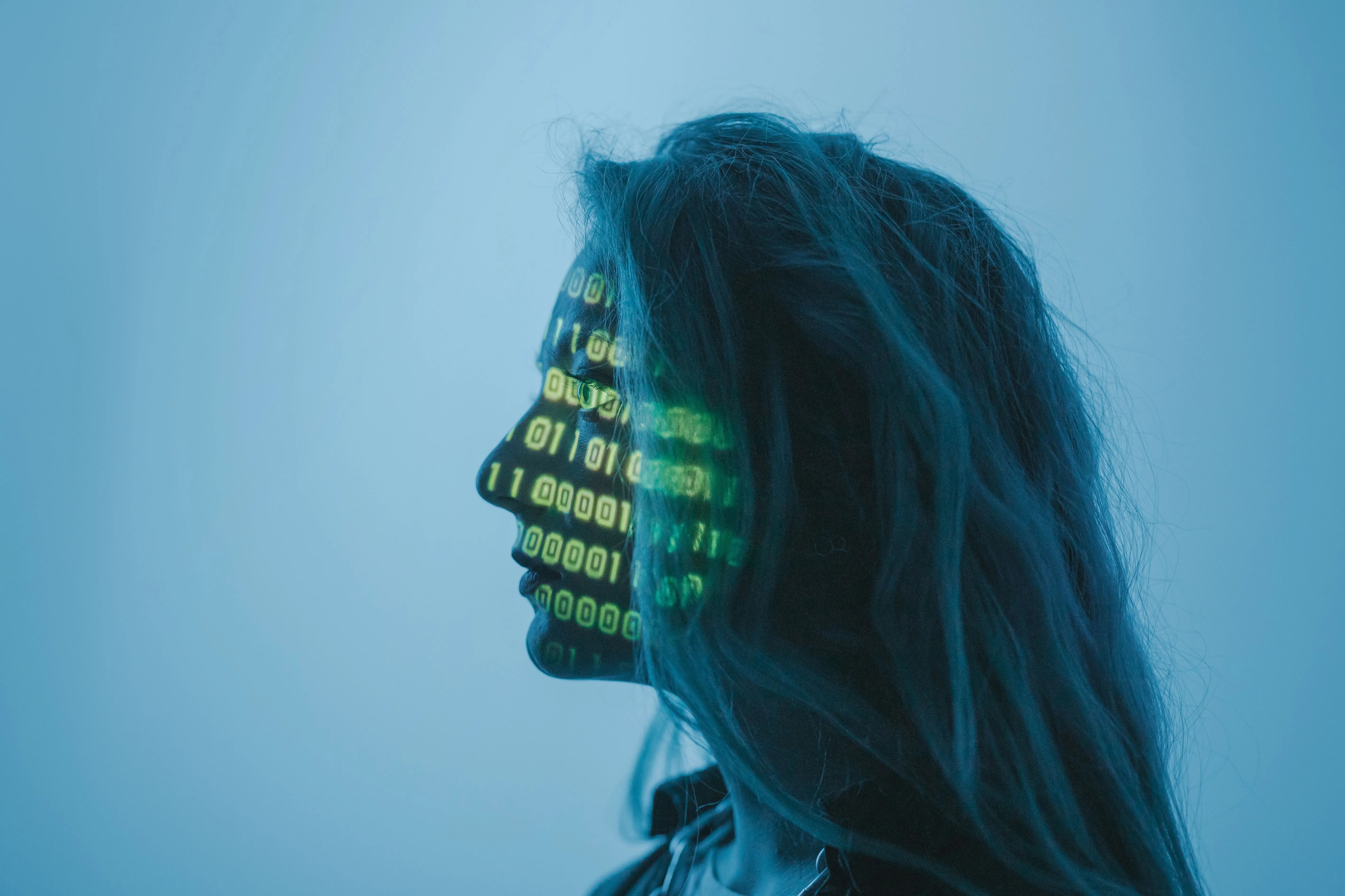 A woman in profile against a blue background, with green binary code projected across her face.
